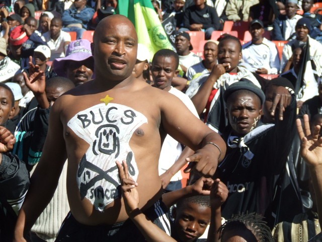 Orlando Pirates supporters in the stands, flags and scarves raised at Orlando Amstel Arena